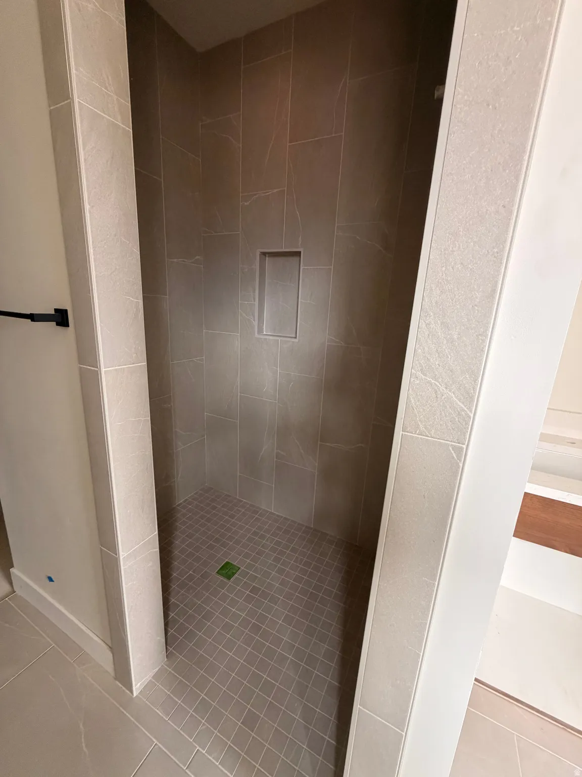 Walk-in shower featuring large format wall tiles, a recessed niche, and smaller grid-patterned floor tiles