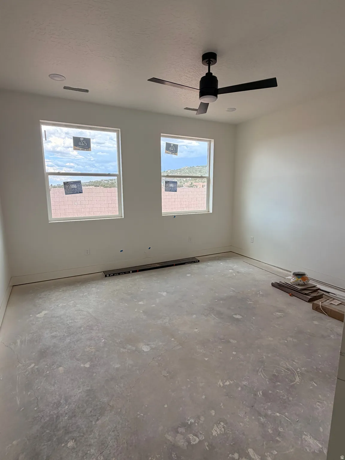 Spacious interior room featuring two large windows, a modern black ceiling fan with integrated lighting, and recessed ceiling lights
