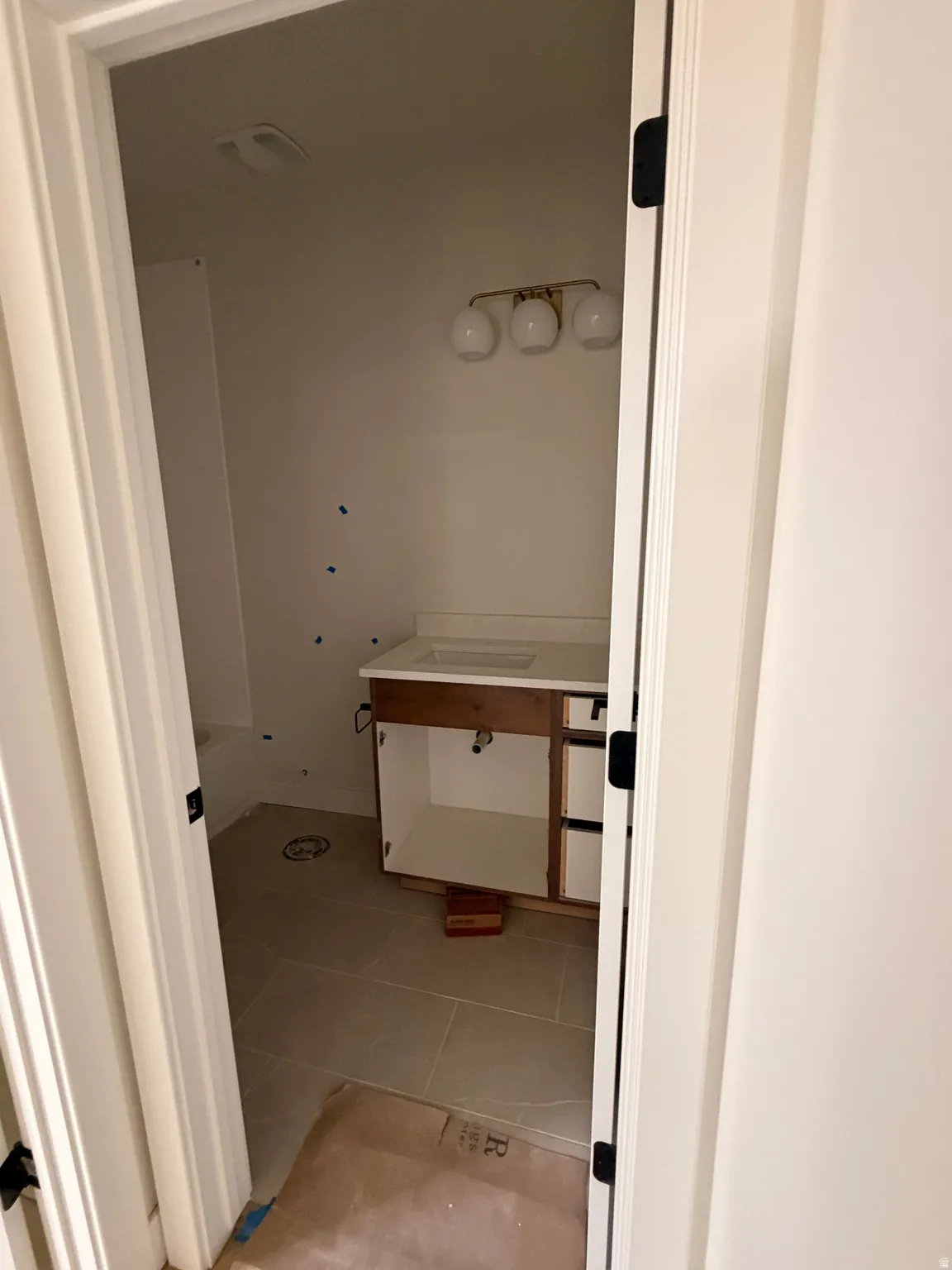 Bathroom featuring neutral floor tiling, a white built-in bathtub, and a vanity with a white countertop and gold-toned light fixture