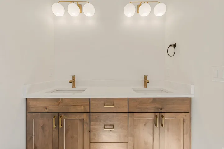 Double vanity with a light wood-finish cabinet base, white countertops, and dual undermount sinks
