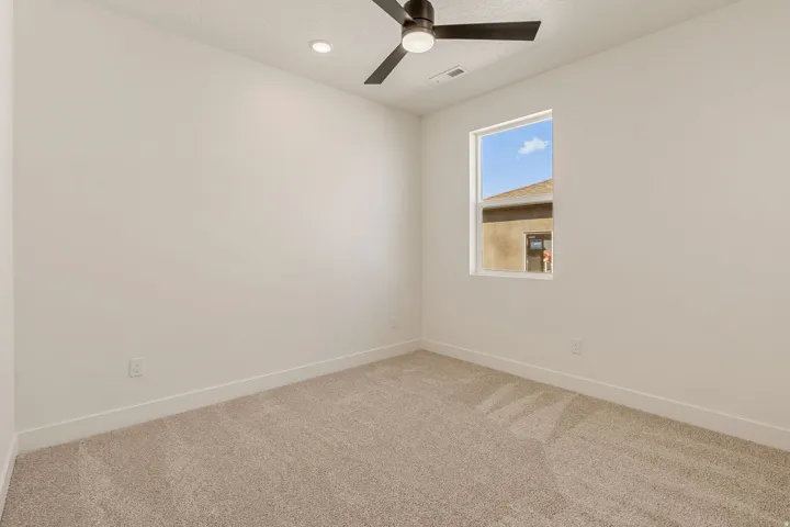 Carpeted room featuring a single window, a ceiling fan with integrated lighting, and a recessed ceiling light