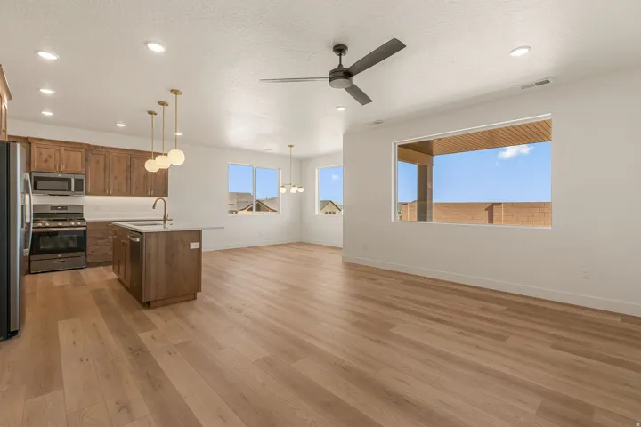 Open-concept living area featuring wood-finish flooring, a contemporary kitchen island with a sink, recessed lighting, and a modern ceiling fan