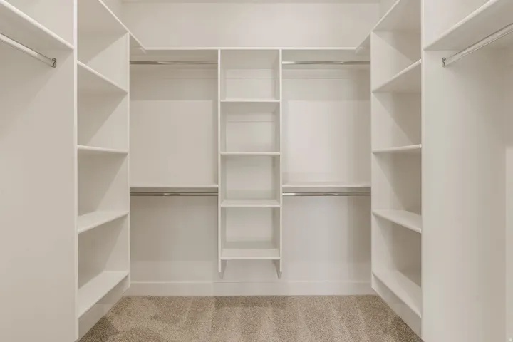 Spacious walk-in closet featuring custom white cabinetry with multiple shelving sections, dual hanging rods, and a carpeted floor