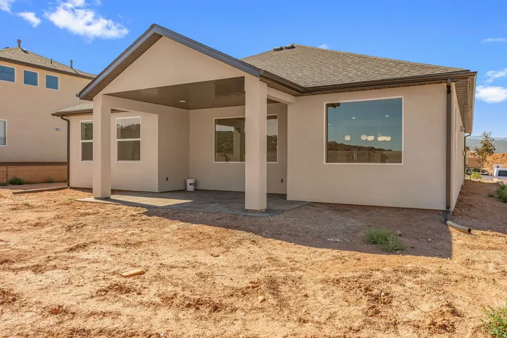 Rear exterior featuring a covered patio with a paver surface, stucco siding, a shingle roof, and multiple windows