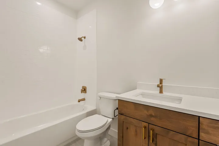Bathroom featuring a white subway tile shower surround, a white bathtub, and a modern vanity with a wood-finish base, integrated sink, and gold-tone fixtures