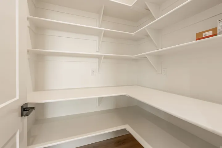 Spacious walk-in pantry featuring multiple levels of white shelving, wood-finish flooring, and integrated electrical outlets