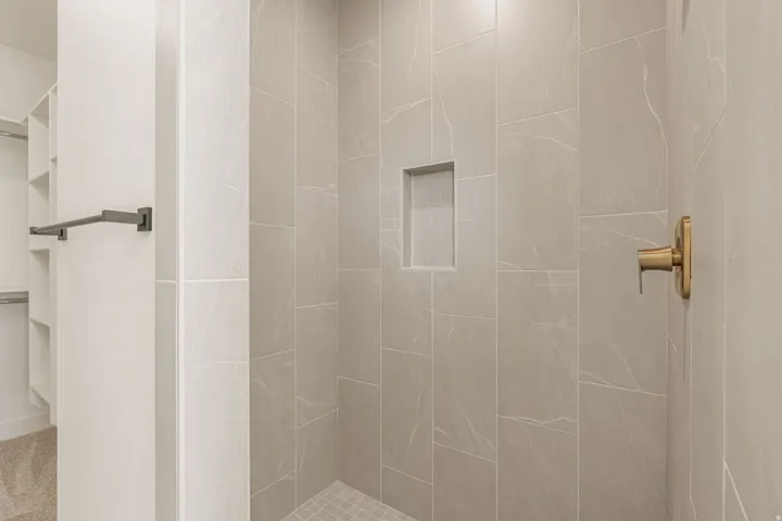 Spa-inspired shower featuring large-format porcelain tile walls with linear pattern detailing, a recessed niche for convenient storage, brushed gold hardware, and a seamless tile floor