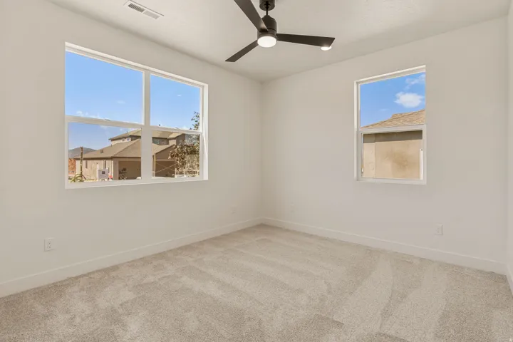 Bright room featuring two windows, neutral carpeting, white walls, a contemporary ceiling fan with integrated lighting, and white baseboards