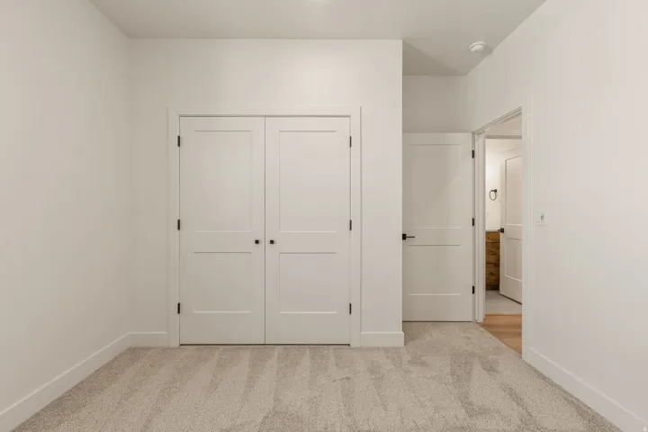 Spacious bedroom featuring dual white panel closets with solid hardware, neutral carpet flooring, and clean white walls with recessed ceiling lighting