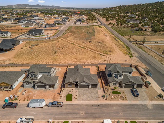 Aerial perspective showcasing multiple residential properties, including a completed home with a dark gray roof and light-colored siding