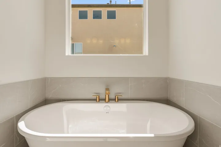 Freestanding soaking tub with gold-finish fixtures and light gray tile surround