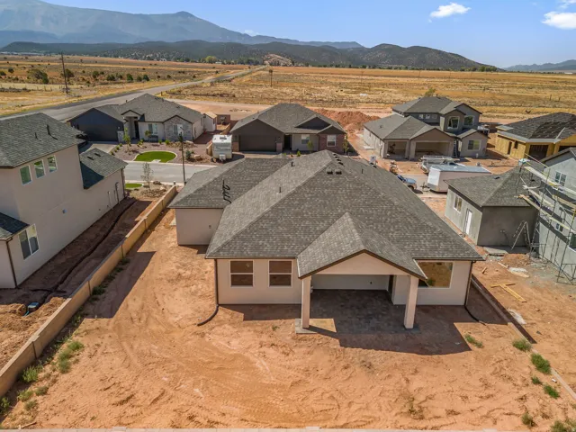 Newly constructed residence featuring a covered patio with paver flooring, a dark gray shingle roof, and light-colored stucco exterior walls