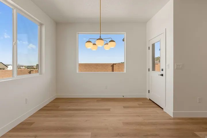 Light wood-finish flooring complements crisp white walls in this bright room, featuring a modern chandelier, large windows, and a white paneled door with glass inserts
