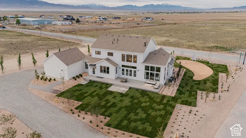 White two-story home with a light brown shingle roof, expansive multi-pane windows, and a concrete patio