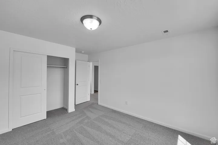 Bedroom featuring light gray patterned carpet, white walls, a flush-mount ceiling light fixture, and a sliding door closet with a hanging rod