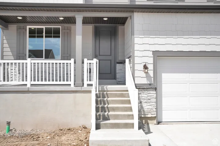 Modern facade featuring shaker siding, a covered front porch with white railing, and a paneled garage door