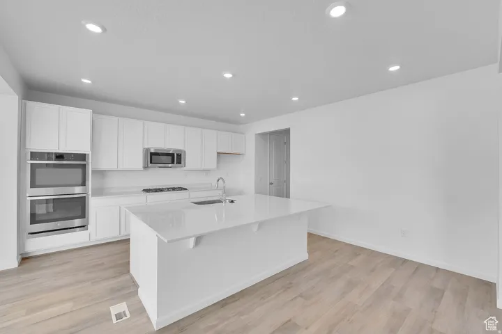 Contemporary kitchen featuring white cabinetry, a large kitchen island, stainless steel appliances, recessed lighting, and wood-finish flooring