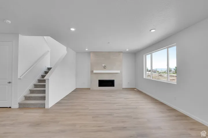 Spacious living area featuring wood-finish flooring, a stone-clad fireplace with a white mantel, and ample natural light from multi-pane windows