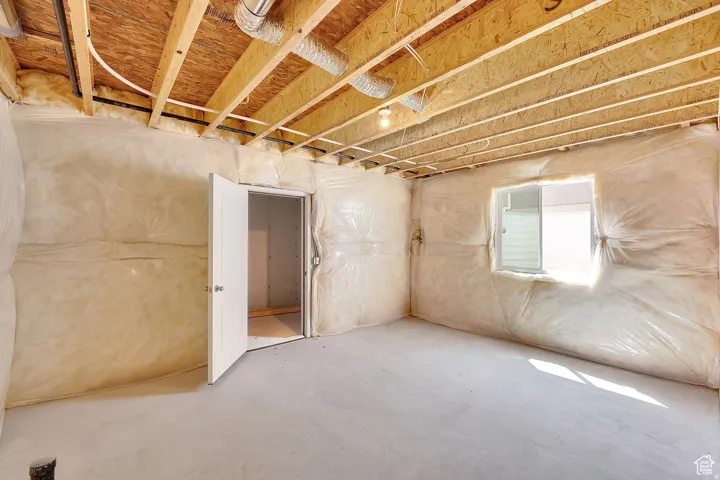 Unfinished basement offering exposed ceiling joists, insulation-wrapped walls, a concrete floor, and a single-pane window