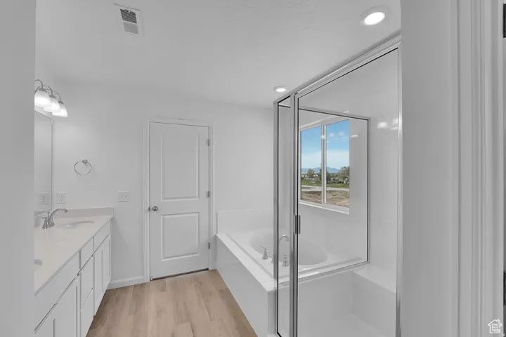 Modern bathroom featuring a glass-enclosed shower, built-in soaking tub, dual vanity with undermount sinks, and wood-finish flooring