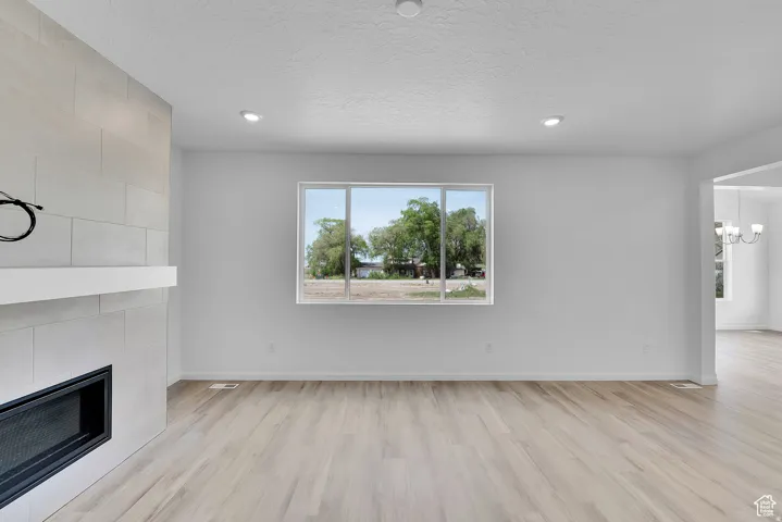 Living space featuring a white tiled fireplace with a built-in firebox, a white mantel, and wood-finish flooring