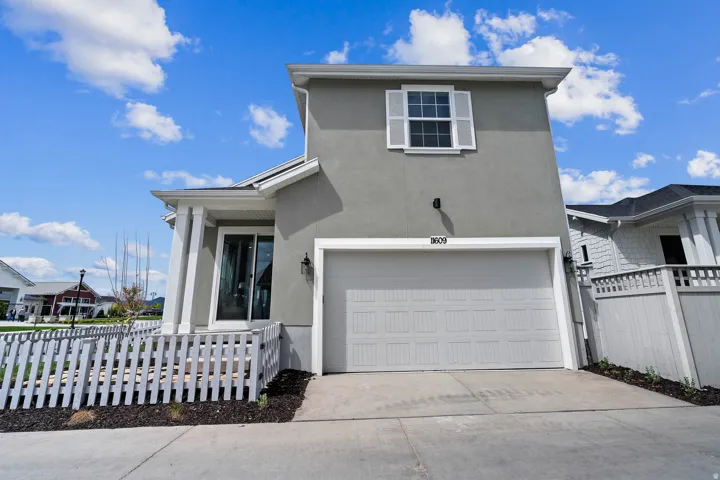 Contemporary facade featuring a light gray stucco finish, an integrated garage, and a white picket fence