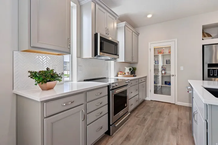 Contemporary kitchen featuring gray shaker-style cabinetry, white countertops, and a white herringbone tile backsplash