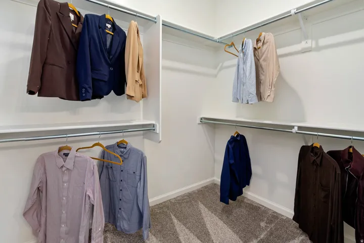 Corner closet system featuring multiple hanging rods, white shelving, and light gray patterned carpeting