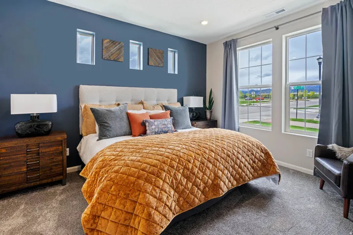 Carpeted bedroom featuring a textured accent wall, two large windows with grid patterns, and a tufted fabric headboard
