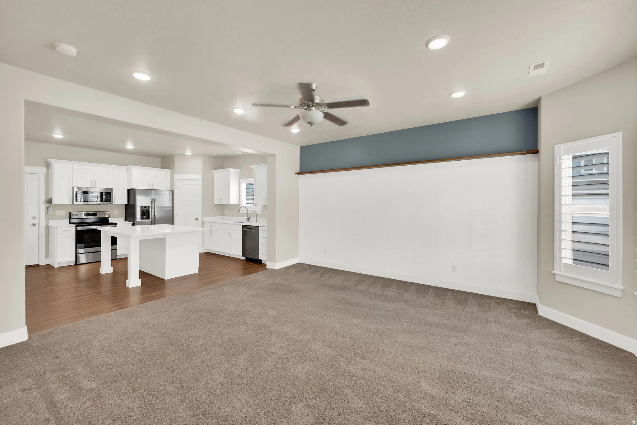 Open-concept living space featuring a kitchen with white cabinetry and stainless steel appliances
