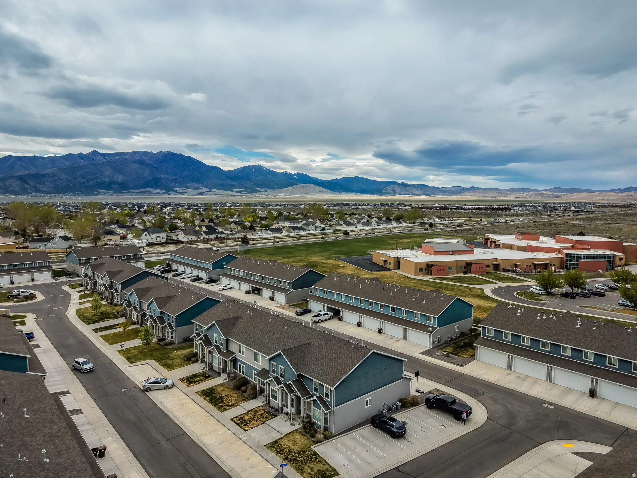 Aerial panorama featuring a residential development composed of multi-story townhomes with garages, surrounded by expansive landscaping