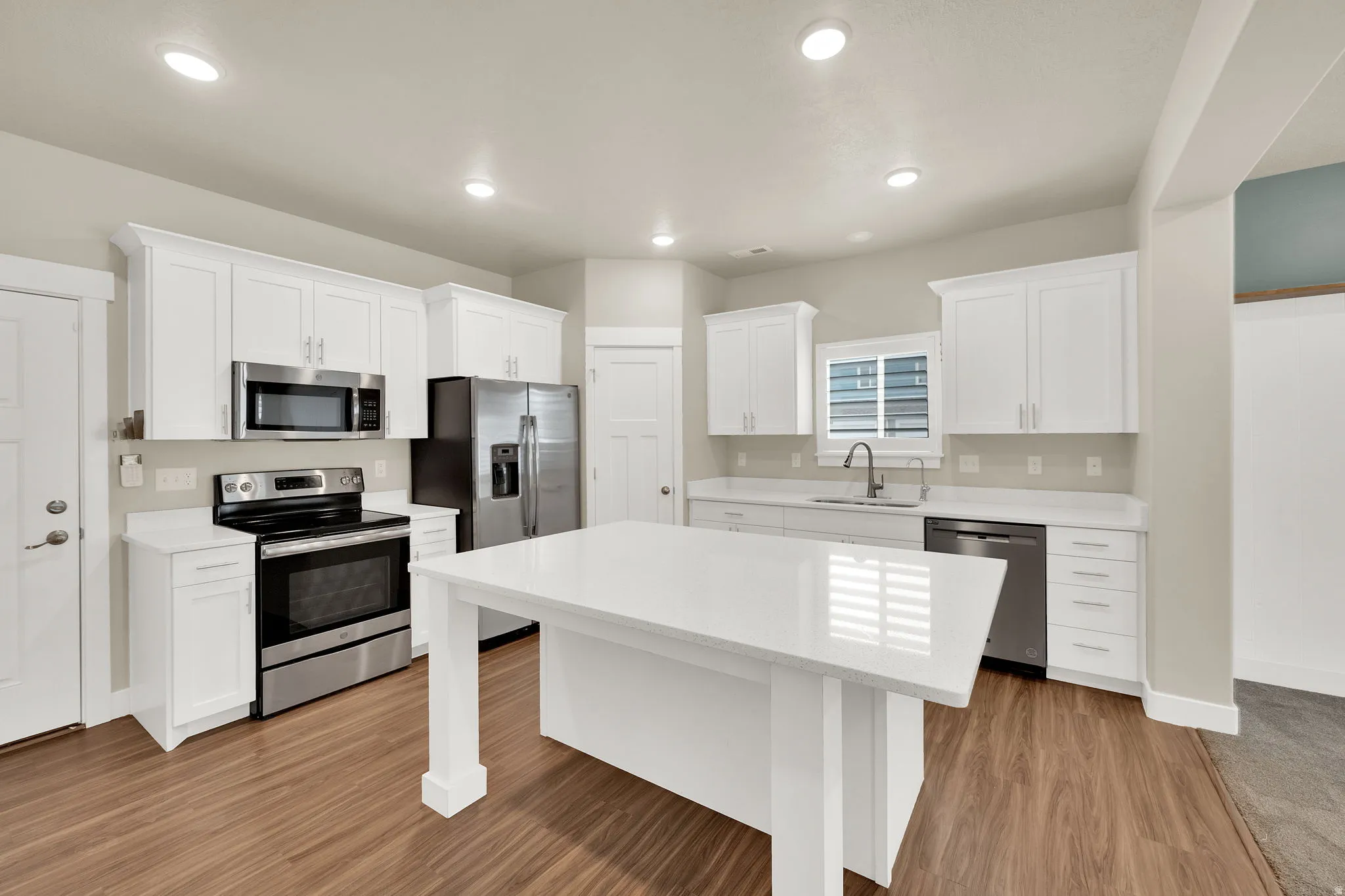 Kitchen featuring a central island with a white countertop, white cabinetry, stainless steel appliances, and wood-finish flooring