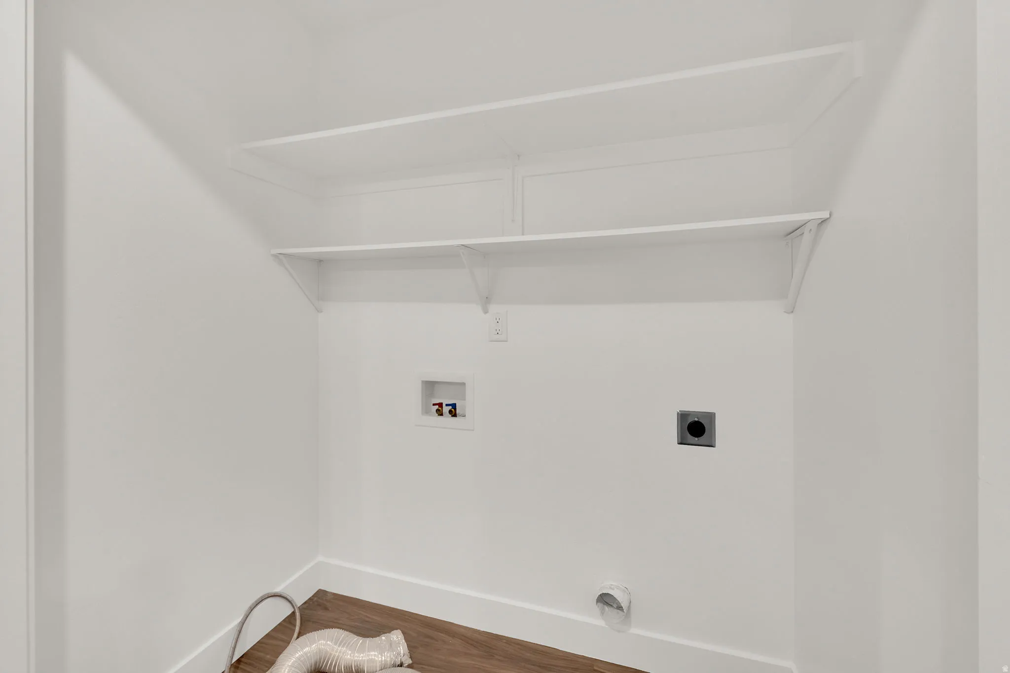 Dedicated laundry area featuring wood-finish flooring, white baseboards, and bright white walls