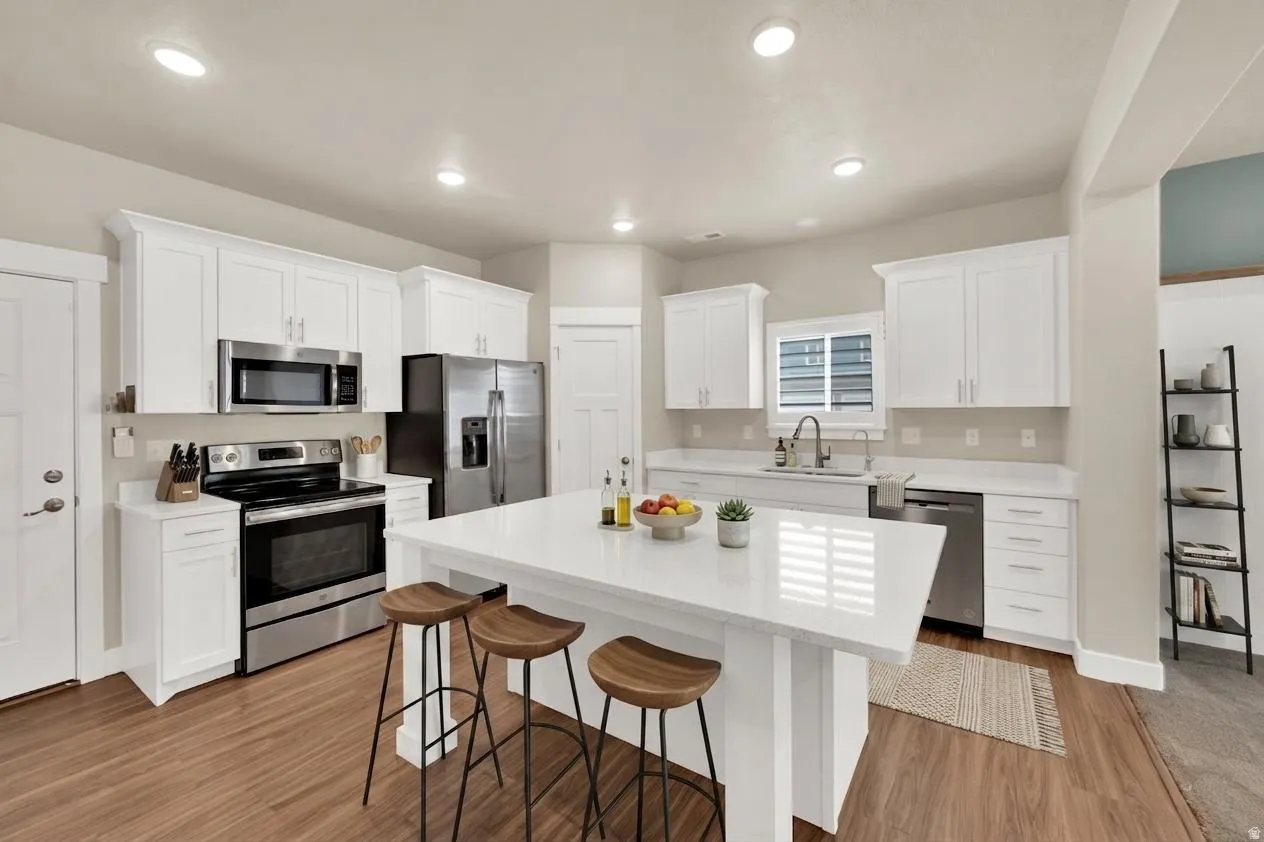 Modern kitchen featuring a central island, white cabinetry, stainless steel appliances, wood-finish flooring, and recessed lighting