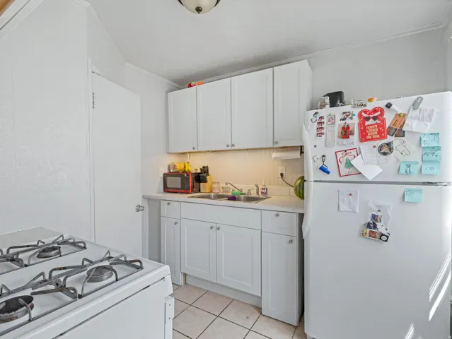 Kitchen featuring white cabinetry, a white refrigerator, a white gas range, and white tile flooring