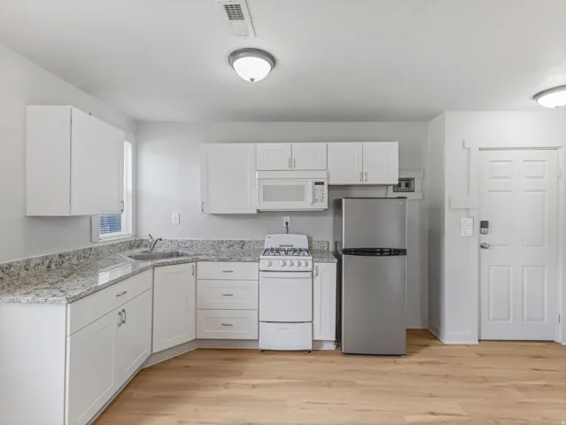 Compact kitchen featuring granite-style countertops, white shaker cabinetry, stainless steel refrigerator, white gas range, and LVP flooring