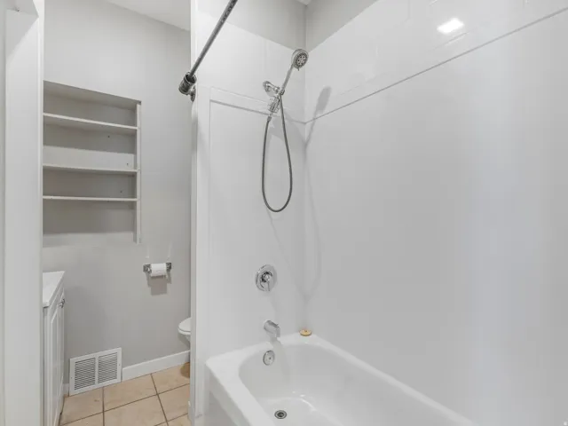 White bathtub with chrome fixtures, full tile surround, and an industrial-style shower curtain rod