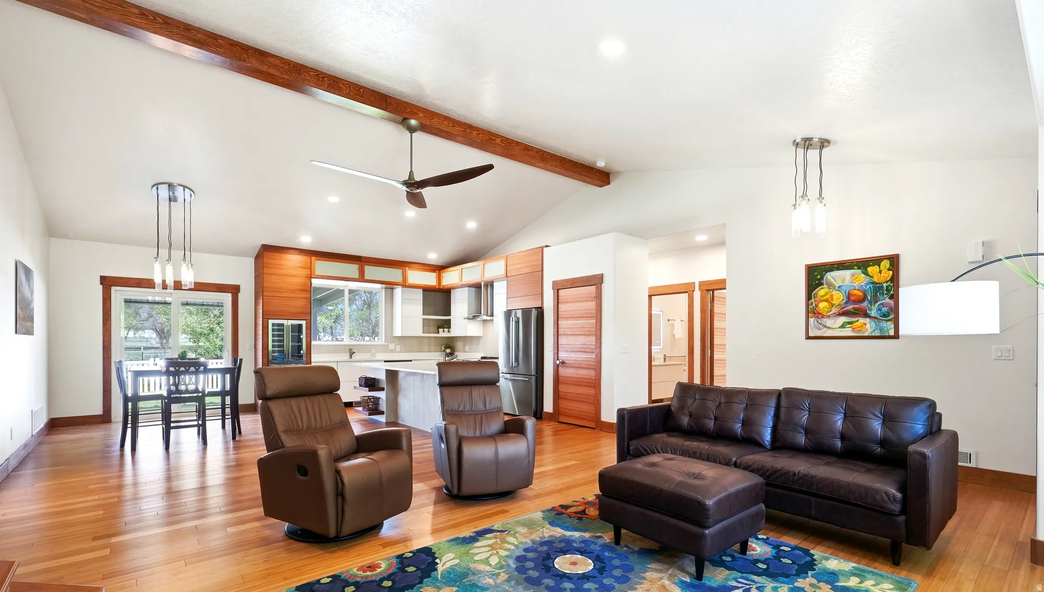 Bright open-concept living, dining, and kitchen area featuring soaring vaulted ceilings with an accent wood beam, recessed lighting, and abundant natural light throughout