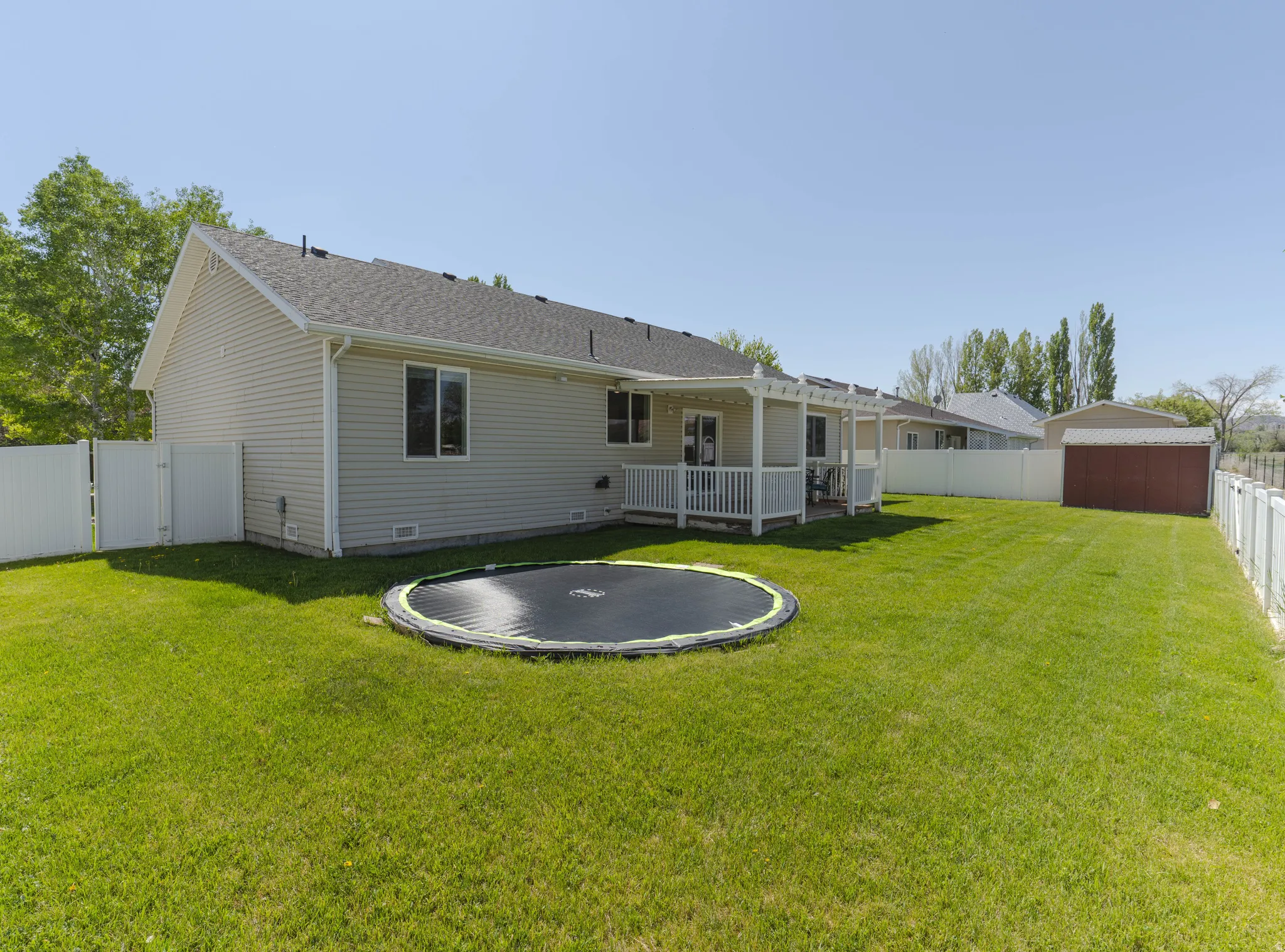 Expansive backyard featuring a manicured lawn, full vinyl privacy fencing, a covered patio, in ground trampoline (included), and an additional storage shed