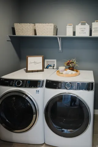 Dedicated laundry space featuring a white front-load washer and dryer set, a wall-mounted shelf, and neutral-toned wall paint