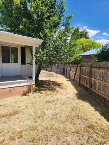 Exterior side yard with a wooden privacy fence, mature trees, and a residential structure featuring a covered porch