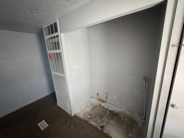 Utility alcove featuring exposed plumbing, electrical outlets, and a textured ceiling