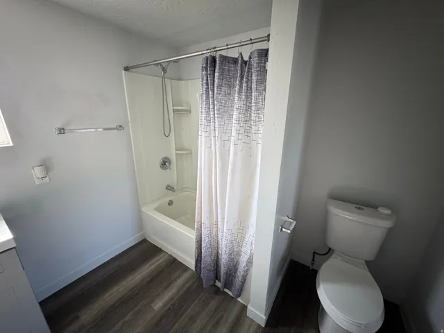 Bathroom featuring a tub and shower combination with a white surround, chrome fixtures, and dark wood-finish flooring