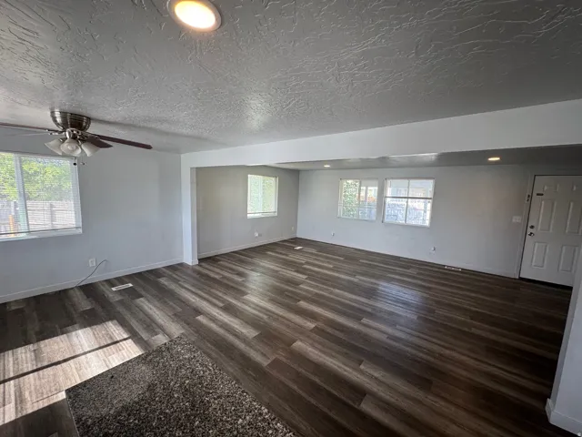Spacious interior featuring wood-finish flooring, light gray walls, multiple windows, and a ceiling fan