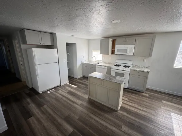 Kitchen featuring an island, light gray cabinetry, white appliances, speckled countertops, and wood-finish flooring