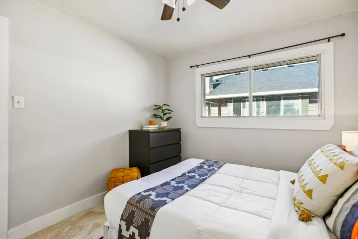 Bright room featuring light grey walls, white trim, a large window with a black curtain rod, and a ceiling fan with wood-finish blades