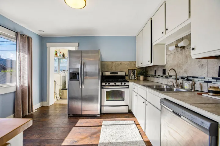 Kitchen featuring stainless steel appliances, white cabinetry, dark wood-finish flooring, and a tiled backsplash with decorative accents