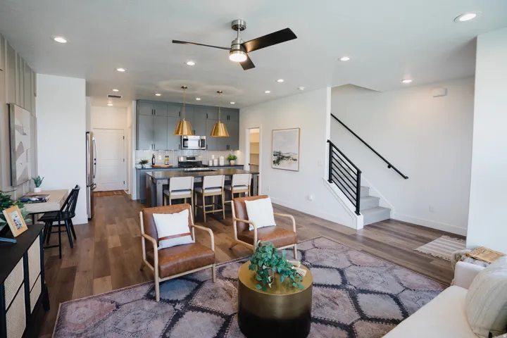 Open-concept living space featuring wood-finish flooring, recessed lighting, a modern kitchen with grey cabinetry, and a contemporary staircase with black railings