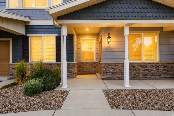 Inviting front porch featuring a decorative outdoor light fixture, stone veneer base, and white support columns