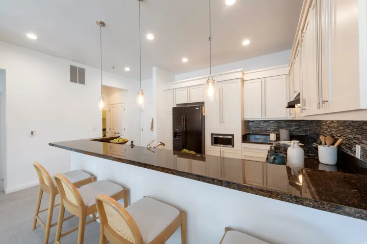 Kitchen featuring a spacious peninsula with dark countertop, white shaker-style cabinetry, and mosaic tile backsplash